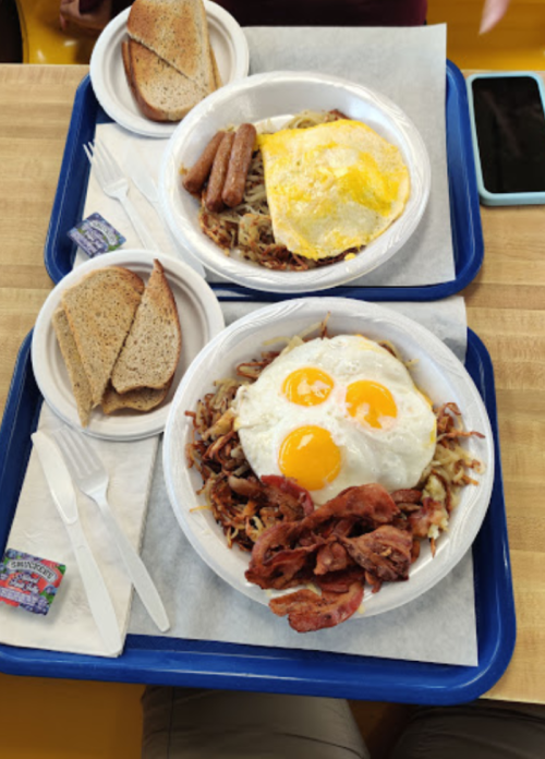 Two trays of breakfast: one with eggs, bacon, and hash browns; the other with sausage, eggs, and toast.