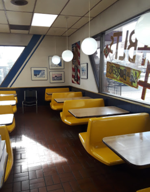 Brightly lit diner interior with yellow booths, round pendant lights, and framed pictures on the walls.