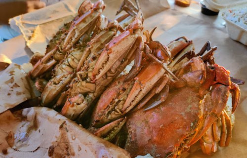 A pile of cooked crabs on brown paper, showcasing their claws and shells in warm lighting.