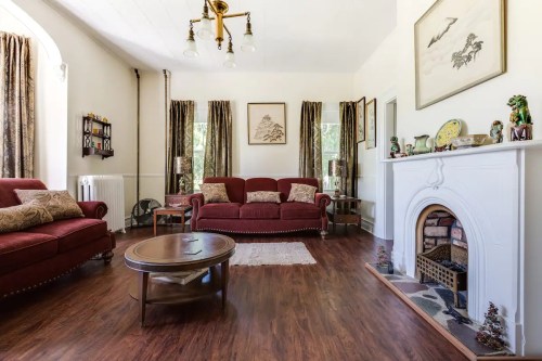 Cozy living room with red sofas, a wooden coffee table, and a decorative fireplace, featuring warm lighting and curtains.