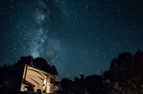 A starry night sky filled with the Milky Way above an RV parked in a serene outdoor setting.
