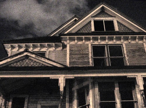 A vintage house at night, featuring multiple windows and intricate architectural details under a cloudy sky.