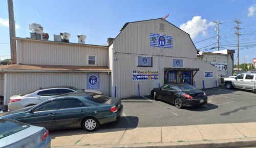 A large, light-colored building with blue signage, parked cars in front, and a clear sky above.