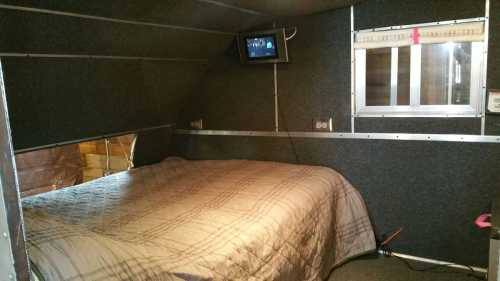 Cozy interior of a camper with a bed, window, and a small TV mounted on the wall.