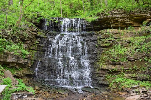 A serene waterfall cascading over rocky cliffs, surrounded by lush green foliage and trees.