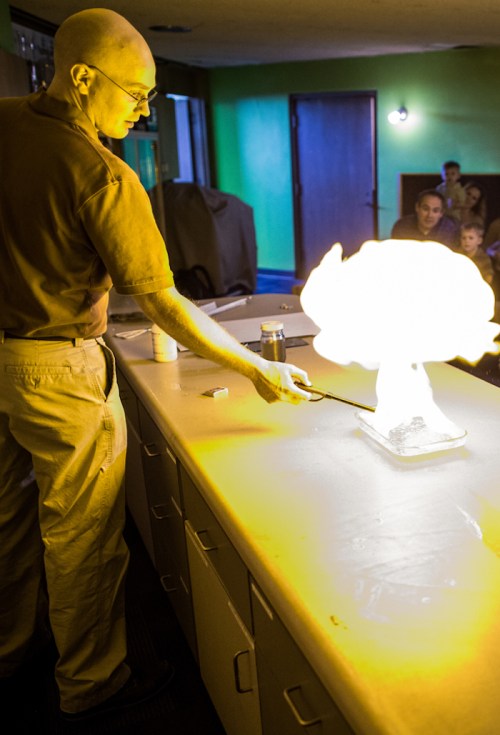 A person demonstrates a science experiment, creating a large flame on a table in front of an audience.