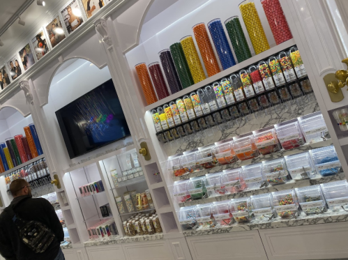 A colorful candy store display with jars of sweets and vibrant candy containers on shelves. A person is browsing.
