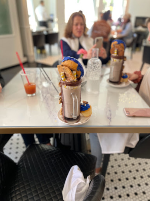 A decadent milkshake topped with cookies and a donut, served on a table with people in the background.
