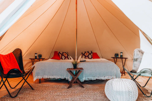 Cozy glamping tent interior with a bed, two chairs, and decorative elements, creating a warm, inviting atmosphere.