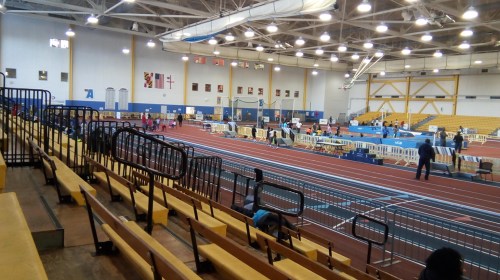 Indoor track and field facility with bleachers, running tracks, and athletes preparing for events.
