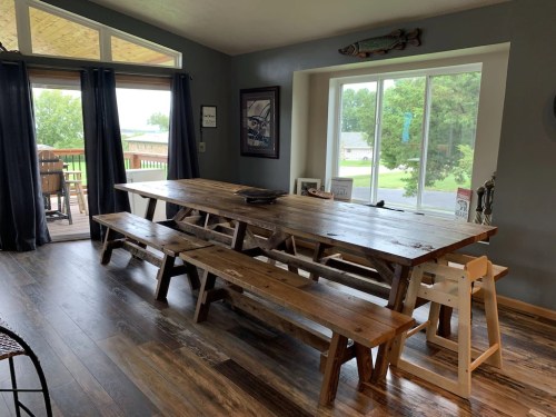 A spacious dining area featuring a large wooden table with benches, large windows, and a view of the outdoors.