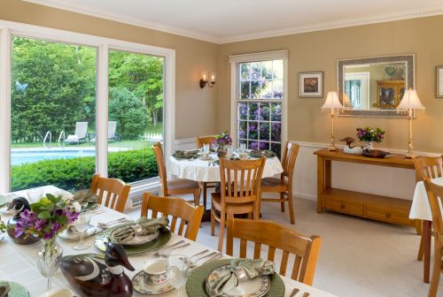 A bright dining room set for a meal, featuring a table with elegant tableware and a view of a pool outside.
