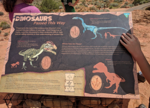 A sign about dinosaurs with illustrations and information about fossil footprints, set in a desert landscape.