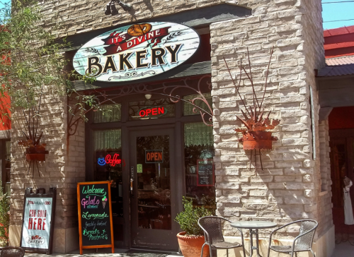 A charming bakery entrance with a sign reading "It's a Divine Bakery," featuring outdoor seating and an open sign.