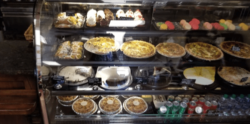A display case filled with various desserts, including cakes, pies, and pastries, alongside colorful macarons and drinks.