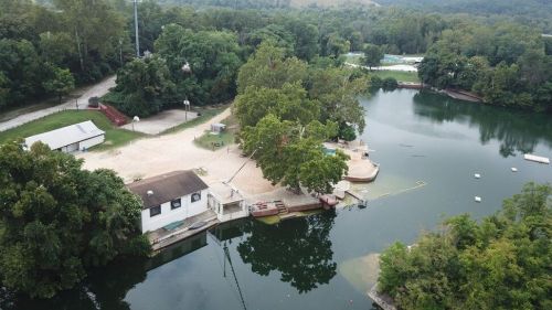 Aerial view of a serene lake surrounded by trees, with a small building and docks along the shore.