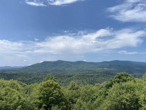 A panoramic view of lush green mountains under a blue sky with scattered clouds.