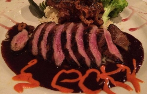 Sliced duck breast on rice, garnished with broccoli and a colorful sauce design on the plate.