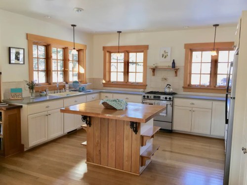 Bright kitchen with wooden accents, large island, stainless steel stove, and multiple windows letting in natural light.