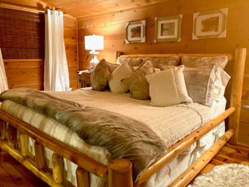 Cozy wooden bedroom with a large bed adorned with plush pillows and a warm blanket, illuminated by a bedside lamp.