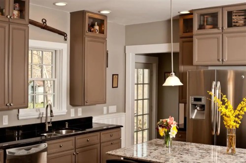 Modern kitchen with dark cabinets, granite countertops, and a vase of yellow flowers on the island. Natural light from windows.