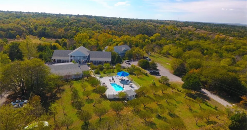 Aerial view of a spacious property with a pool, surrounded by trees and greenery, featuring a large house in the background.