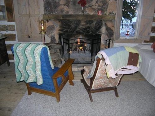 Two cozy armchairs with blankets in front of a stone fireplace, creating a warm and inviting atmosphere.
