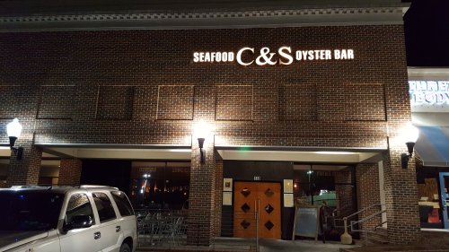 Exterior of C&S Oyster Bar, featuring a brick facade, illuminated sign, and outdoor seating area at night.