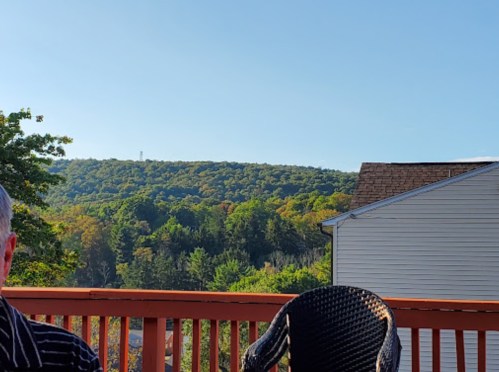 A scenic view of rolling hills and trees under a clear blue sky, with a wooden deck in the foreground.