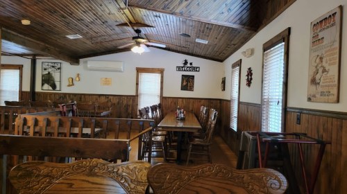 Interior of a rustic restaurant with wooden walls, ceiling fans, and empty tables set for dining.
