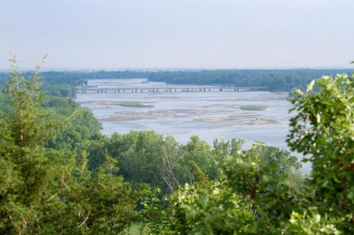 A scenic view of a river winding through lush greenery, with a bridge in the distance under a clear sky.