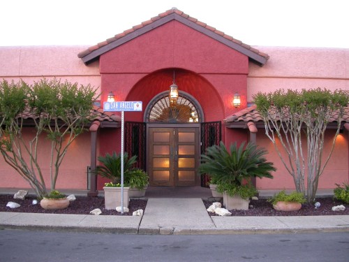 A colorful building entrance with a red facade, arched doorway, and decorative plants on either side.