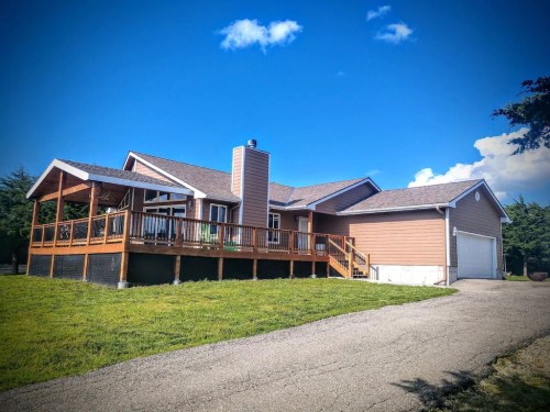 A single-story house with a wooden deck, garage, and green lawn under a blue sky with a few clouds.