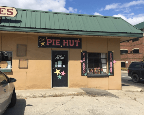 Exterior of "The Pie Hut," a restaurant with a green roof, colorful signage, and a window display.