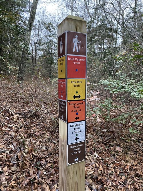 Trail signpost in a wooded area, displaying directions and distances for various hiking trails.
