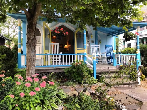 A charming house with blue trim, rocking chairs on the porch, and colorful flowers in the garden.