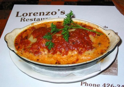 A dish of baked pasta topped with marinara sauce and garnished with parsley, served in a small oval dish.