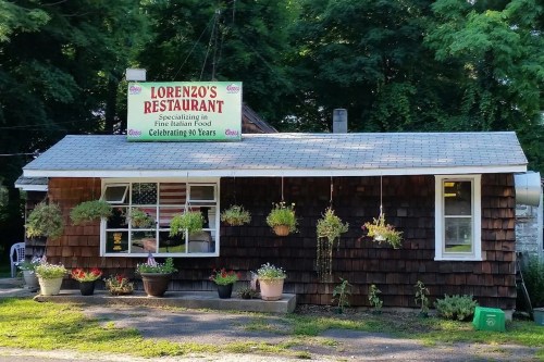 A small restaurant with a sign reading "Lorenzo's Restaurant," surrounded by greenery and flower pots.