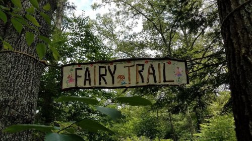 A wooden sign reading "Fairy Trail" surrounded by lush green trees and foliage.