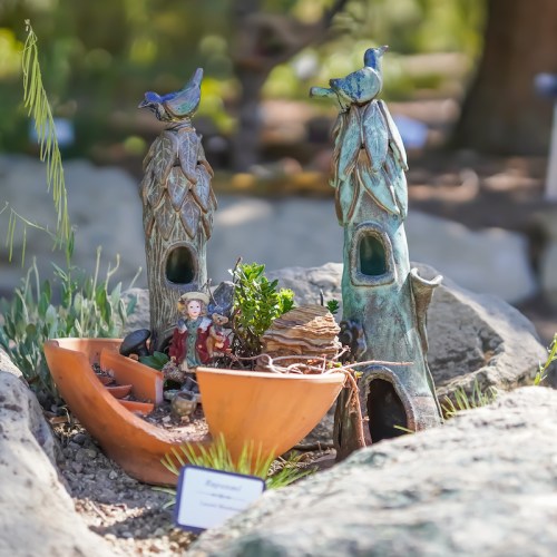 A whimsical miniature garden scene featuring a boat, tiny figures, and decorative birdhouses among rocks and greenery.