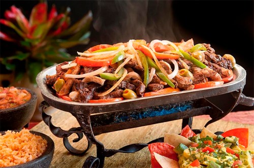 Sizzling platter of grilled meat with peppers and onions, served with rice and fresh salsa on the side.
