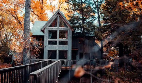 A cozy cabin surrounded by vibrant autumn trees, featuring large windows and a wooden deck.