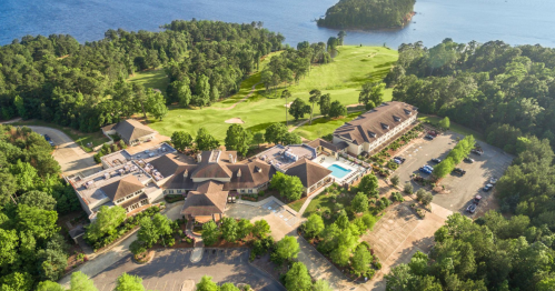 Aerial view of a resort with a pool, surrounded by greenery and a lake, featuring golf course areas nearby.
