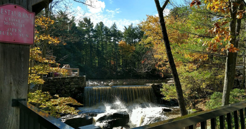 A serene waterfall surrounded by autumn foliage, with a restaurant sign indicating closed hours in the foreground.