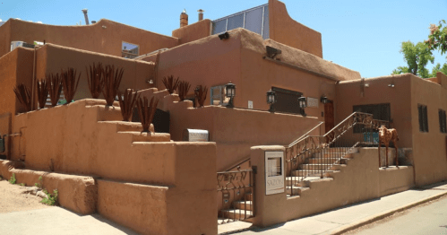 A southwestern-style building with adobe walls, stairs, and decorative plants under a clear blue sky.
