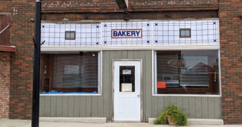 A bakery storefront with a sign reading "BAKERY" and an "OPEN" sign in the window, featuring a brick exterior.