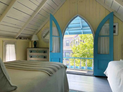 Cozy bedroom with two beds, blue doors open to a sunny balcony, and a view of greenery outside.