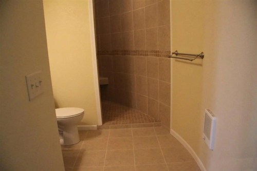 A bathroom featuring a shower, toilet, and tiled walls with a towel rack.
