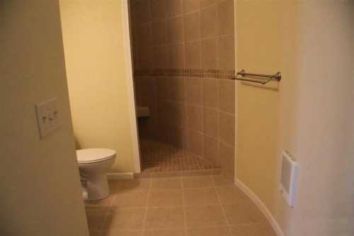 A bathroom featuring a shower, toilet, and tiled walls with a towel rack.