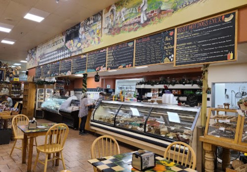 A cozy deli with a display case of food, chalkboard menus, and wooden tables in a warm, inviting atmosphere.